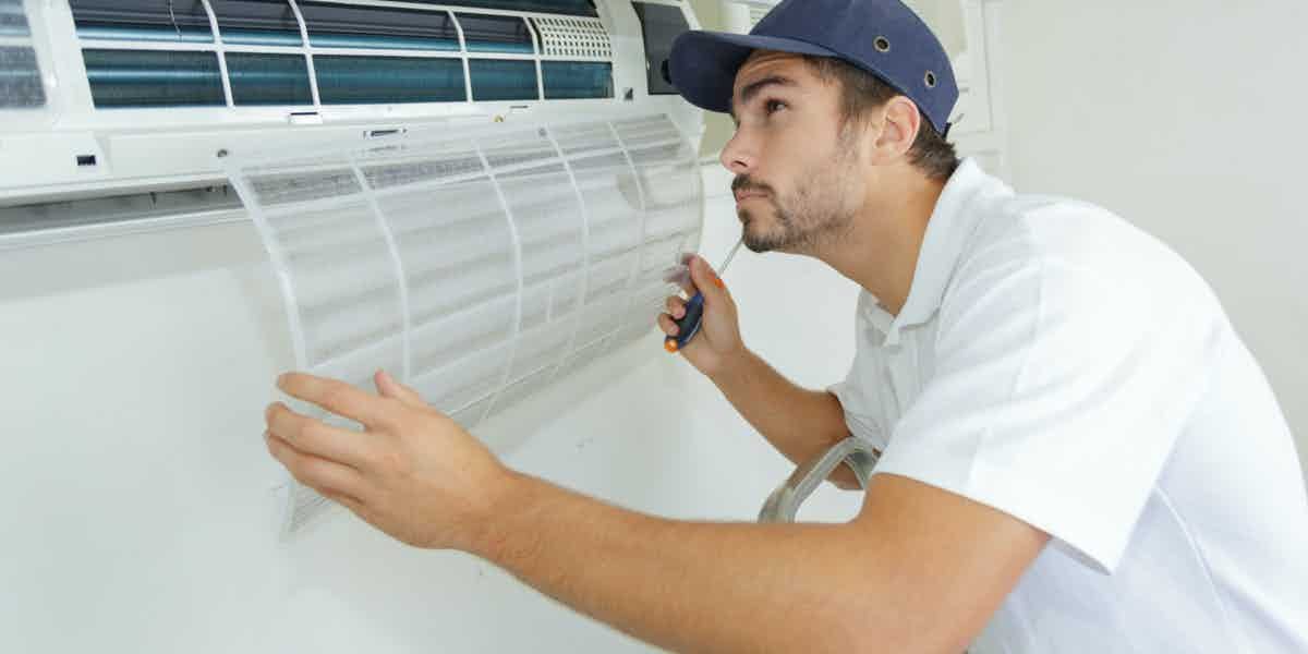 Technician removing a wall air-conditioner filter during indoor AC service