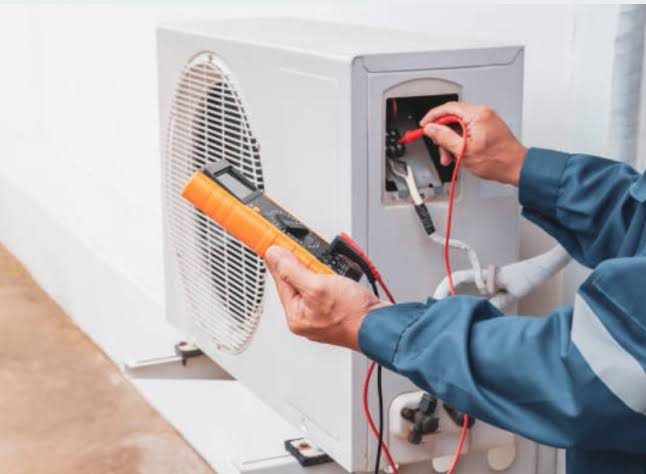 Technician using a multimeter on a compact outdoor air-conditioning unit