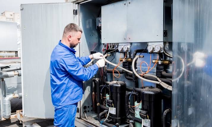 Technician working on rooftop HVAC piping, gauges, and compressors