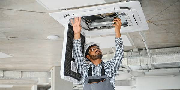 Technician inspecting a ceiling cassette air-conditioning unit
