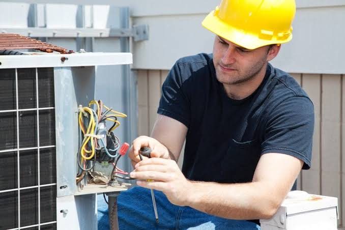 Technician working on outdoor air-conditioner wiring with a screwdriver